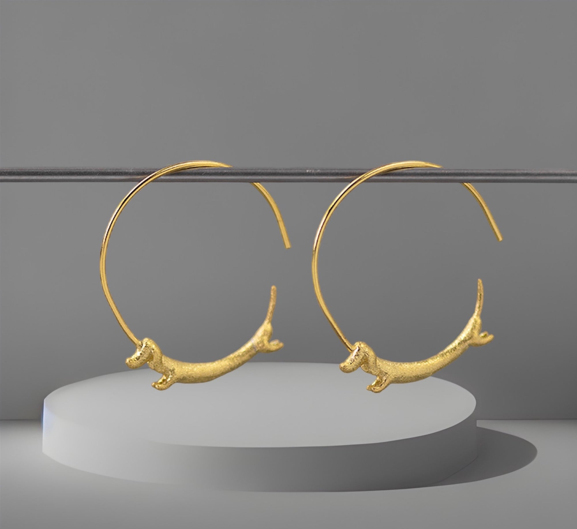 A pair of gold-plated hoop earrings featuring a flying dachshund design with a Chinese zodiac symbol.