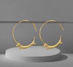 A pair of gold-plated hoop earrings featuring a flying dachshund design with a Chinese zodiac symbol.