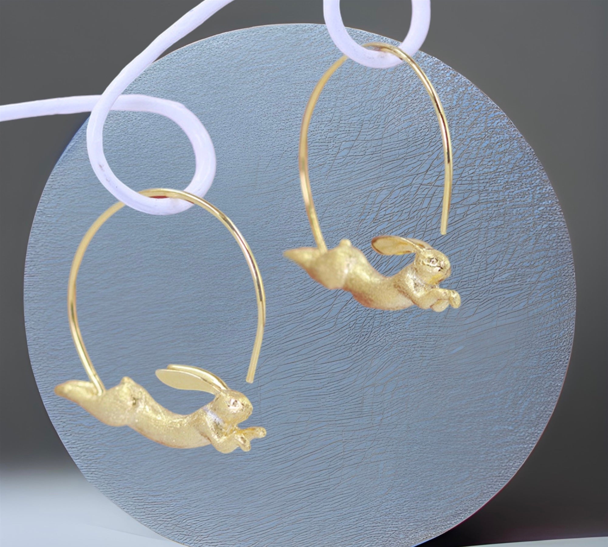 A pair of gold-plated hoop earrings with a silver rabbit design leaping out from the hoop.